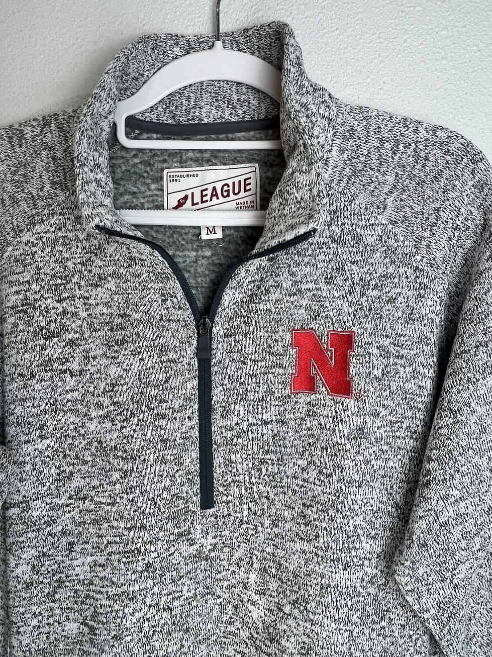 Close-up of Nebraska Huskers logo and League brand tag on quarter-zip fleece.