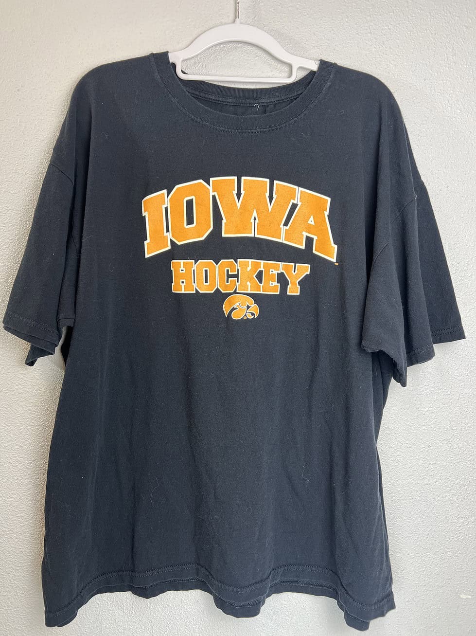 Black Iowa Hawkeyes hockey T-shirt with gold “IOWA HOCKEY” lettering and Hawkeye logo.