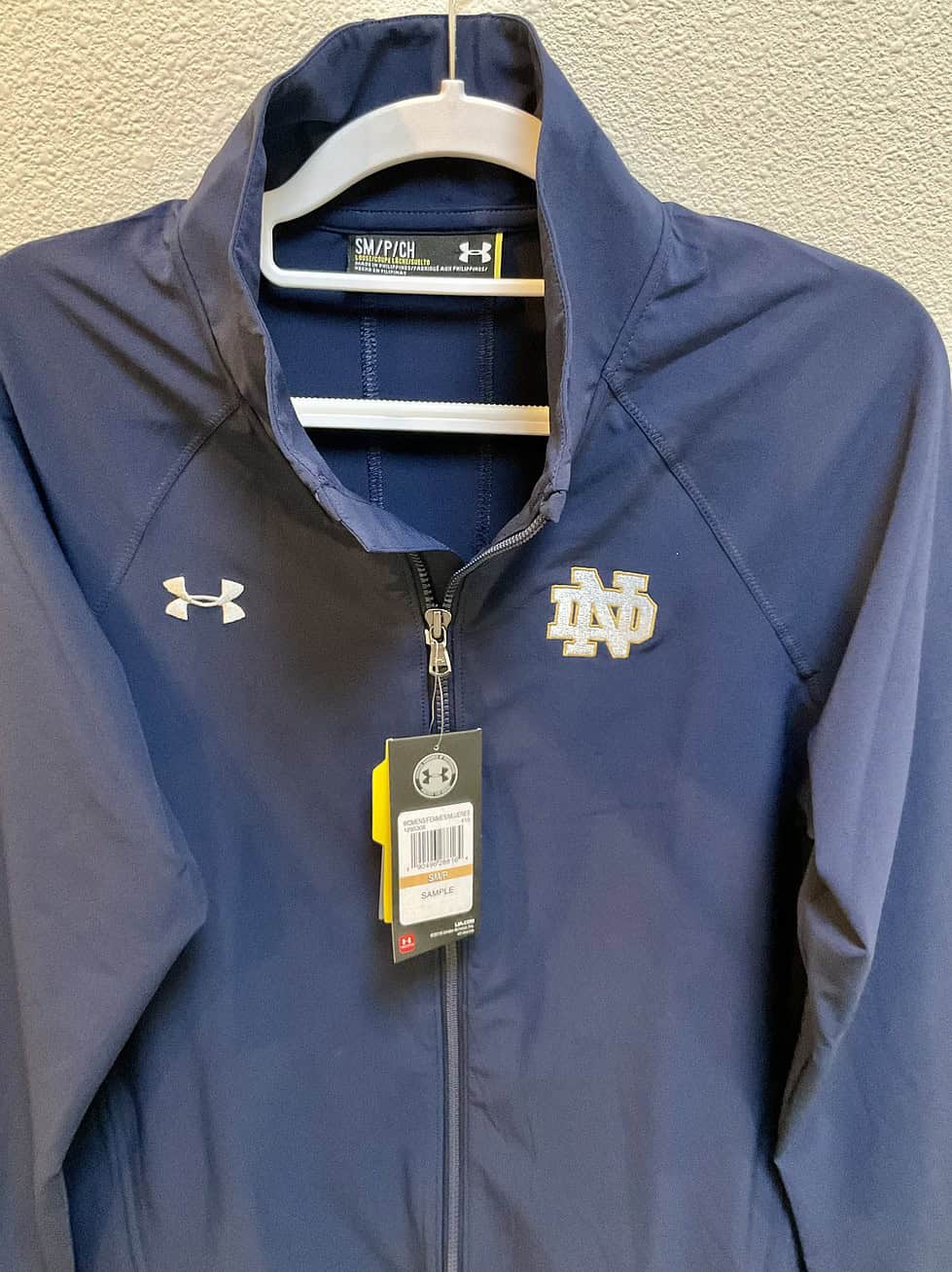 Close-up of Under Armour sample tag on Notre Dame jacket, showing size small and product code.