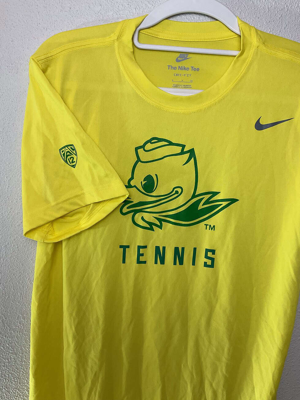 Close-up of University of Oregon Ducks Tennis Nike Dri-FIT tee showing green duck mascot and “TENNIS” print, with Pac12 logo on sleeve