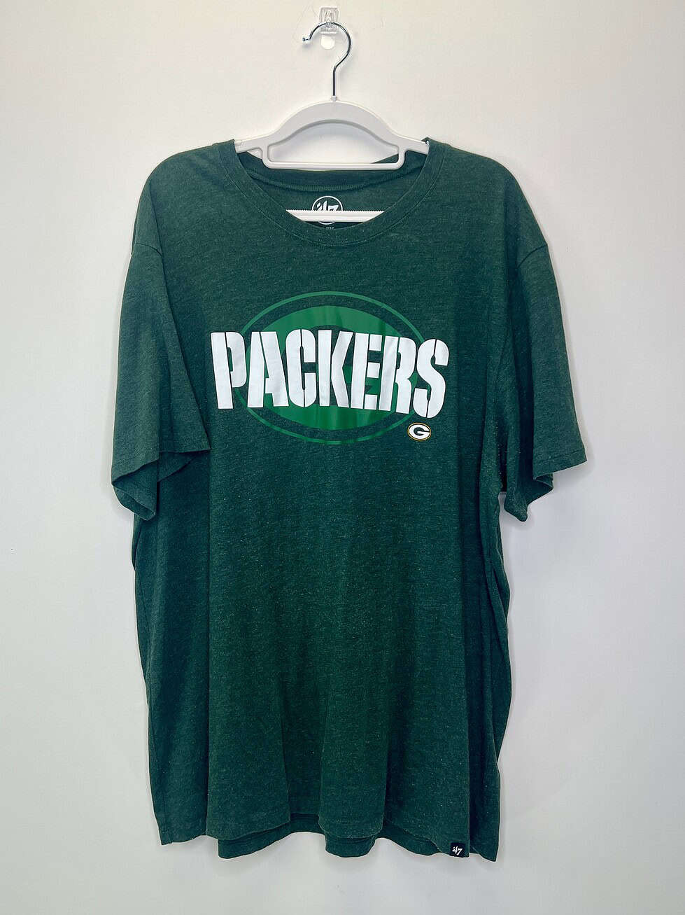 Front and close-up views of a green '47 Brand Green Bay Packers T-shirt in size 2XL, featuring bold “PACKERS” lettering across the chest and a vintage heathered texture.