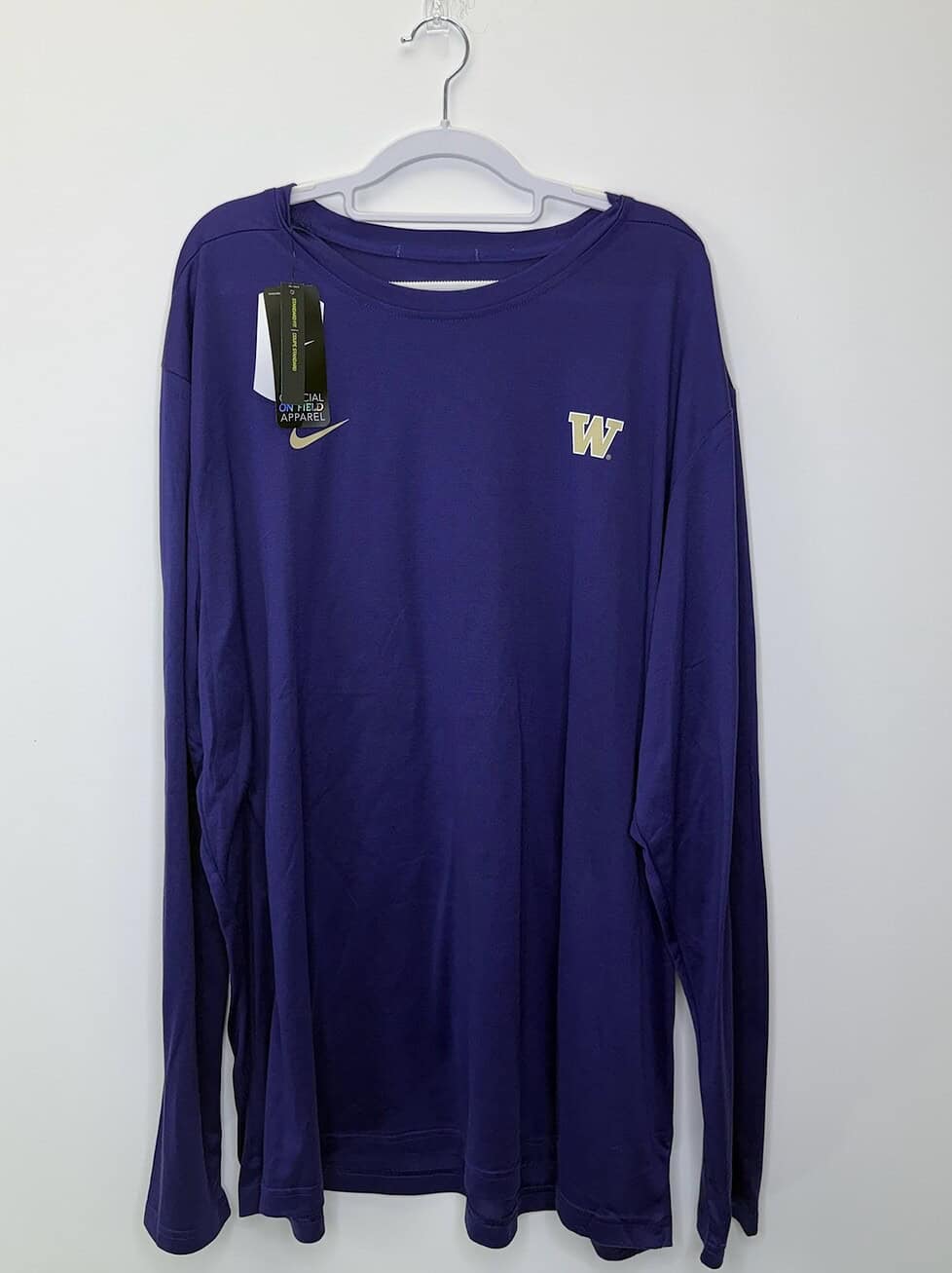 Front views of a purple Nike Dri-FIT long sleeve shirt featuring the Washington Huskies "W" logo and official on-field apparel tags.