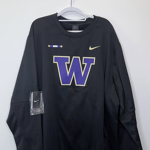 Front and back views of a black Washington Huskies Nike Dri-FIT sweatshirt with gold swoosh and official on-field tag, size 2XLT.